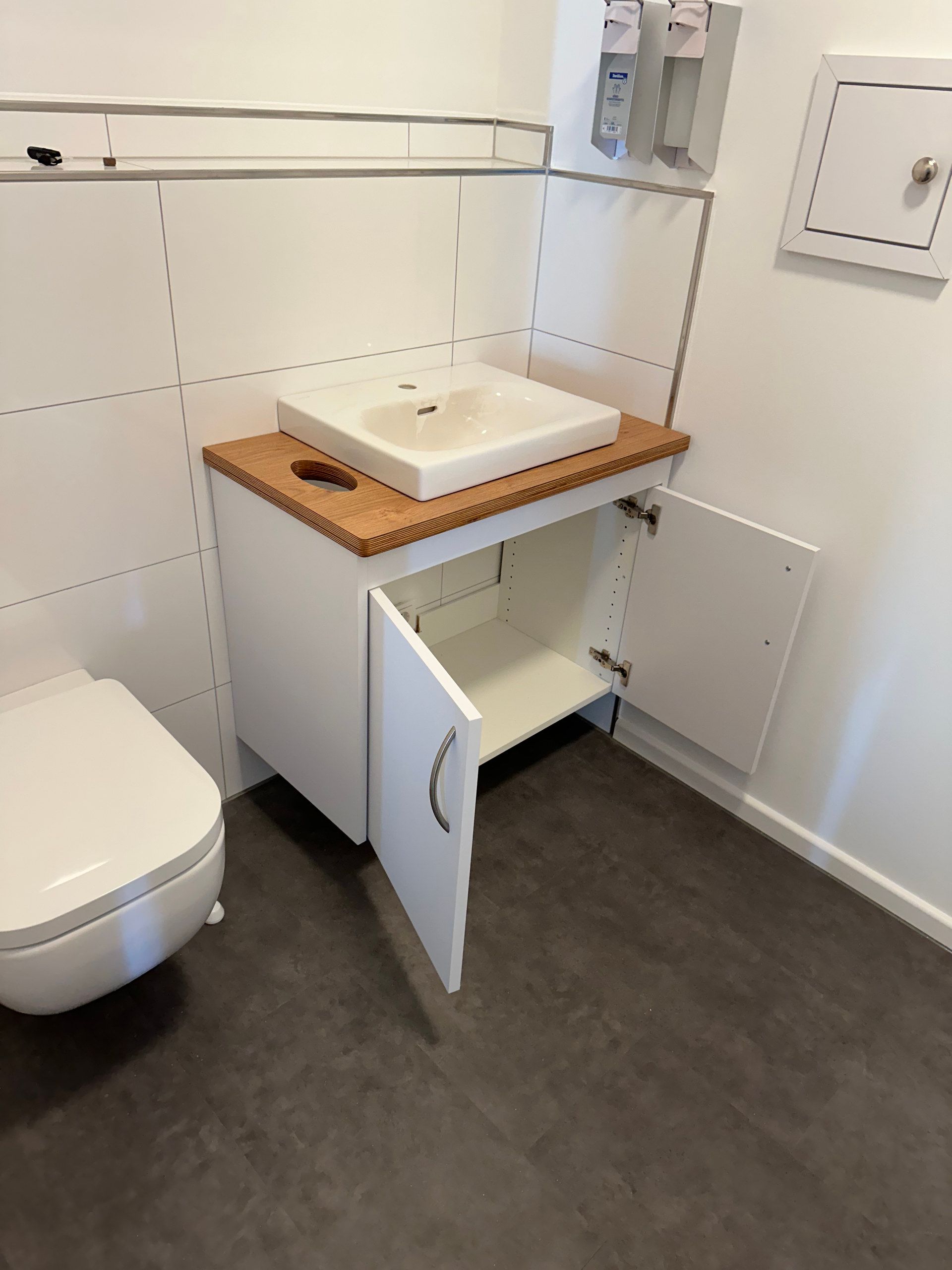 Weißer Waschtischunterschrank mit geöffneter Tür neben dem WC