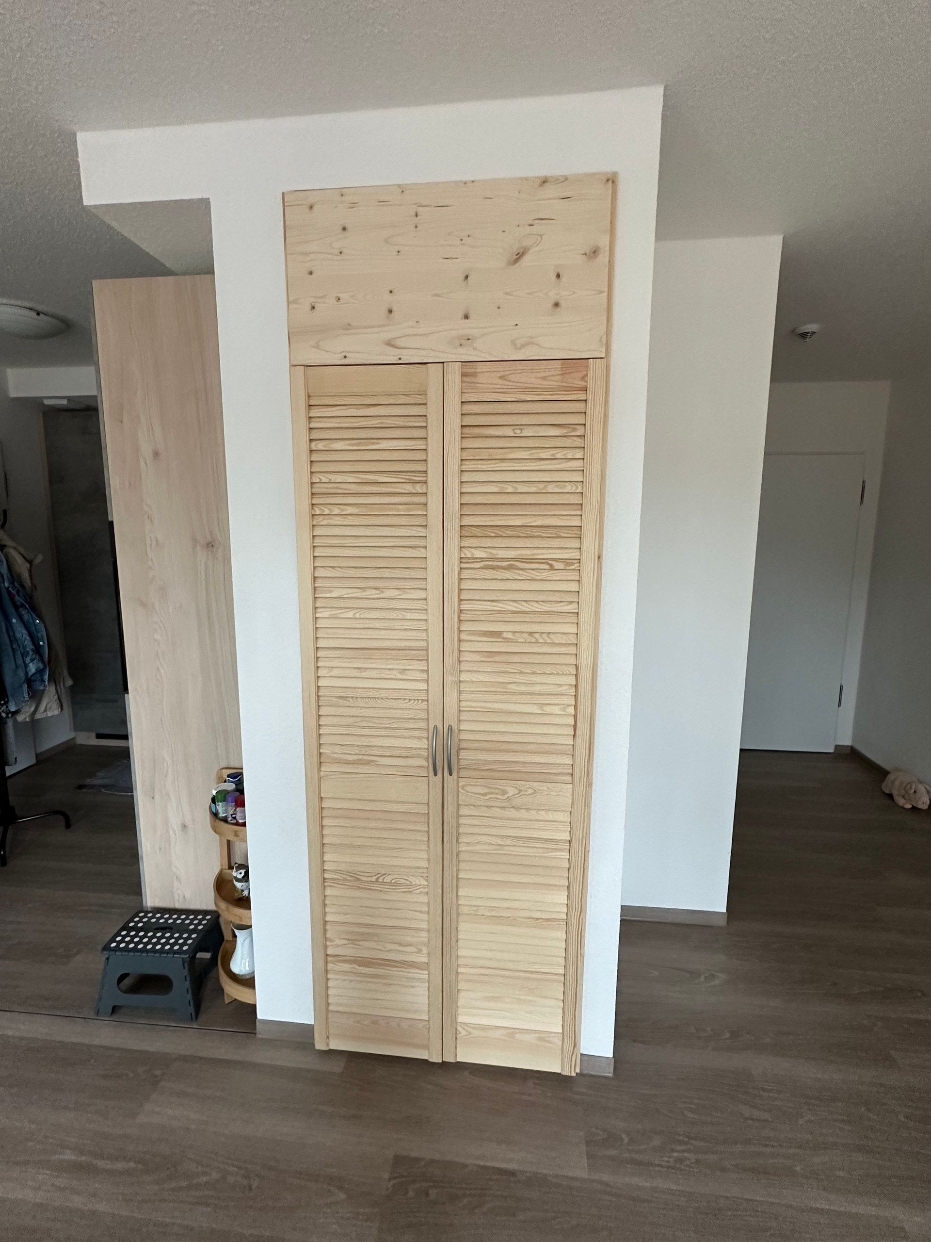 Hochschrank mit Lamellentüren aus hellem Holz in einer Wandnische