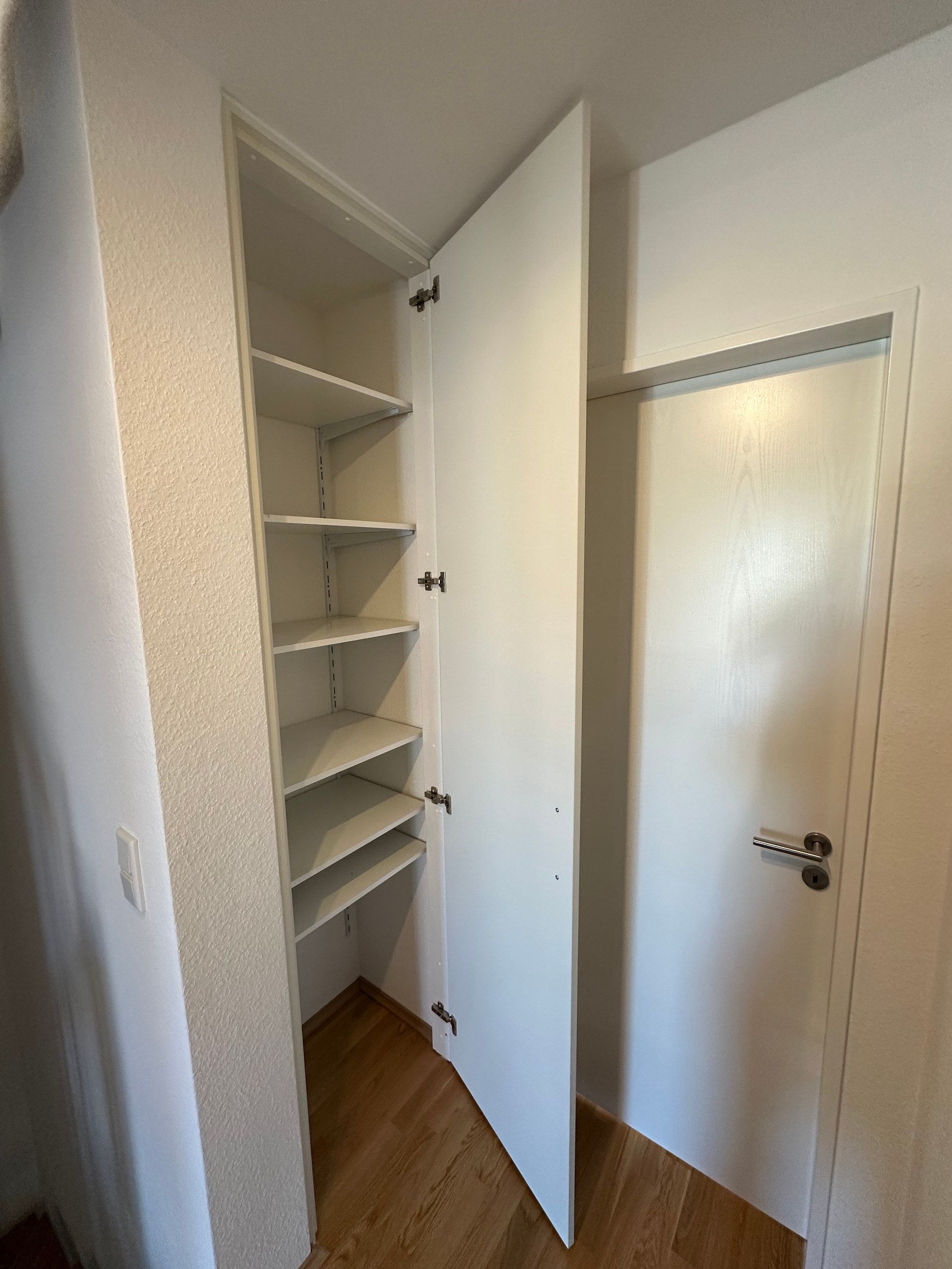 Schmaler weißer Einbauschrank, geöffnet, neben einer Tür