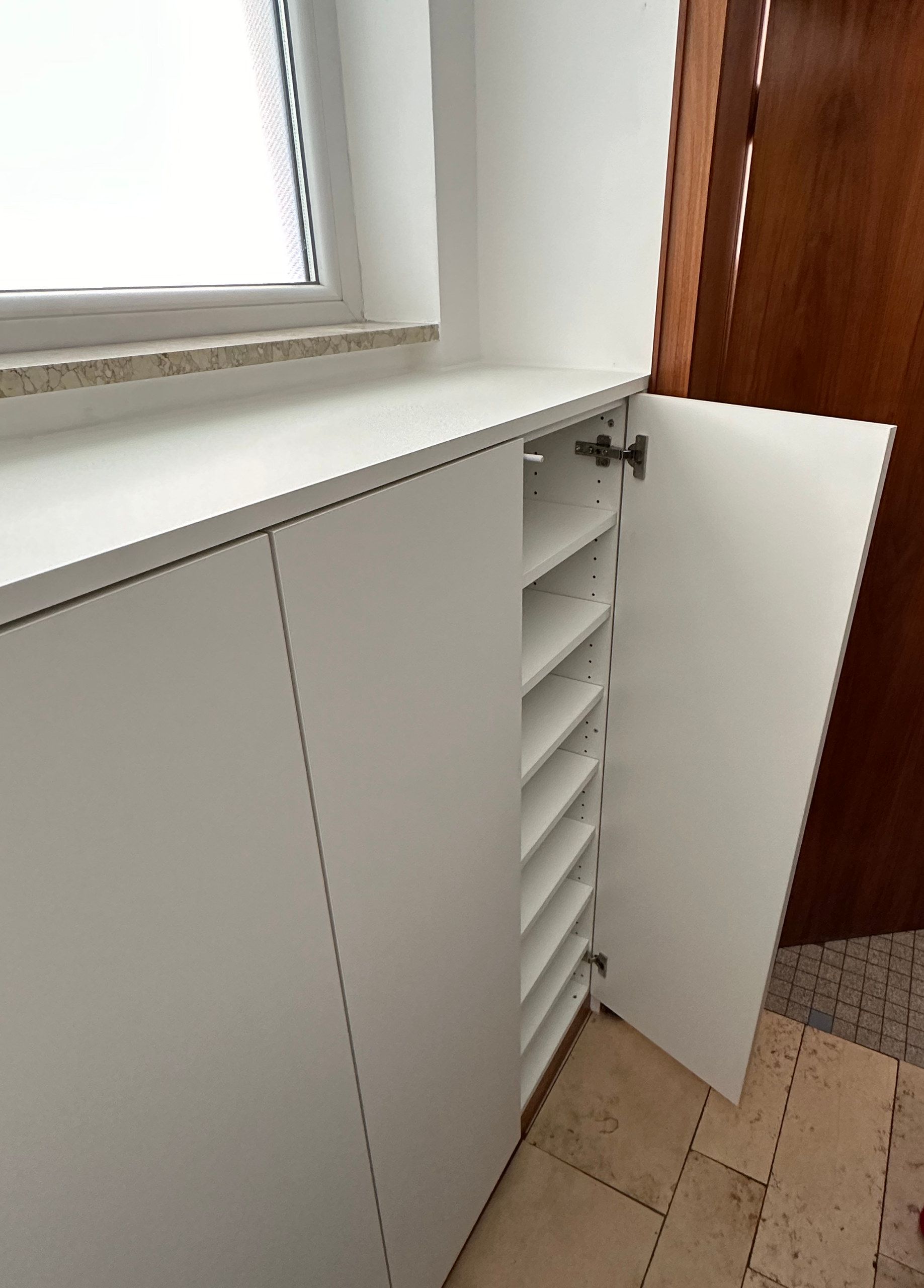 Geöffneter Schrank unter dem Fenster mit Schuhfächern