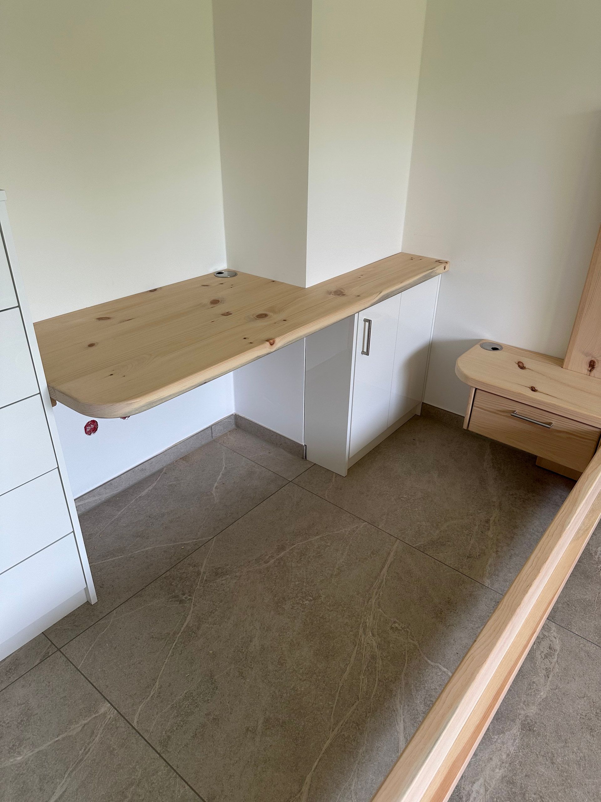 Schreibtischplatte aus hellem Massivholz an der Wand, daneben ein Bettrahmen